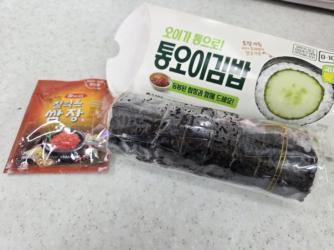종이곽 안에 김밥 한 줄과 쌈장 한 봉지가 있다. 오이를 통째로 넣은 단순한 구성이 특징이다. (사진=한전진 기자)