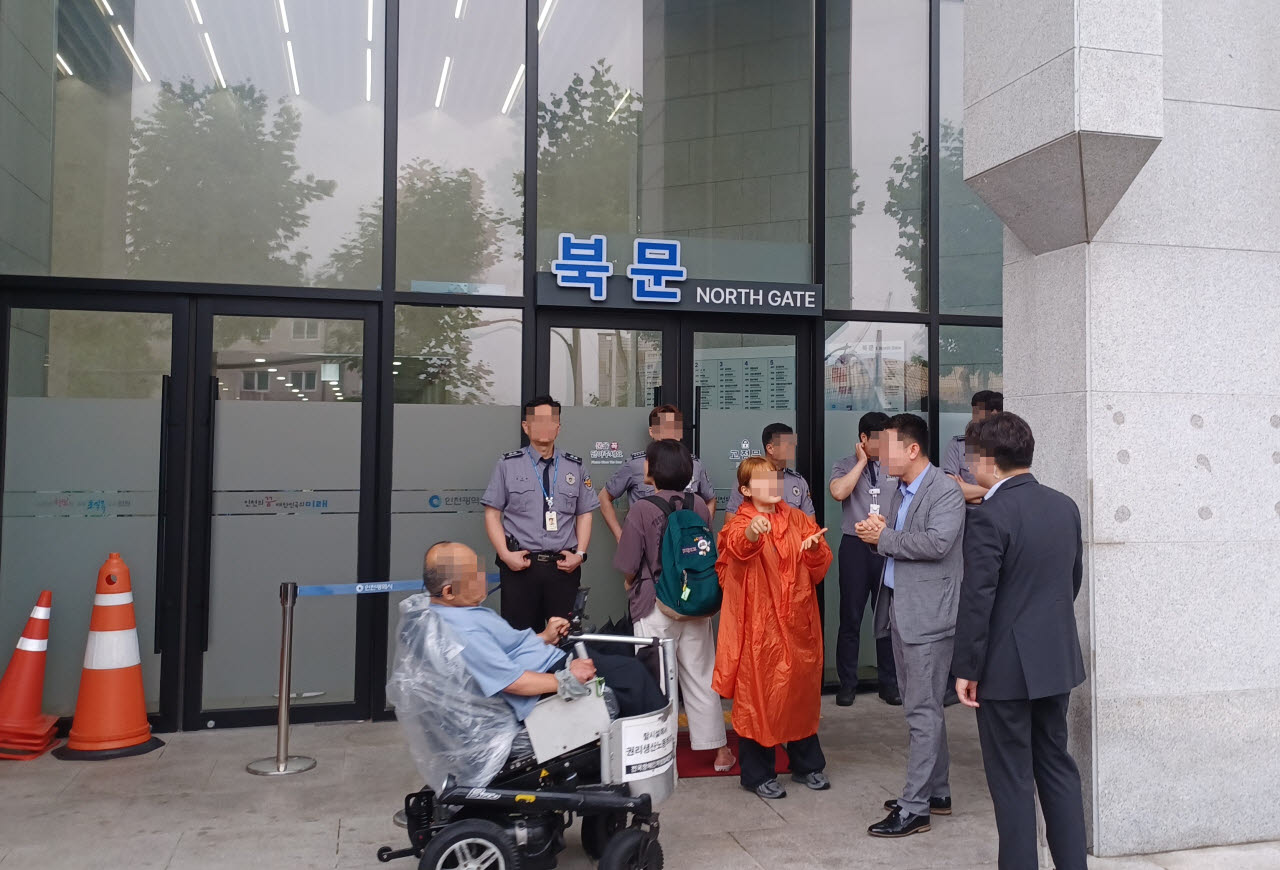 22일 낮 12시30분께 인천시청 북문 앞 진출입 경사로에 고깔 십여개가 놓여 있어 장애인들이 청원경찰관에게 항의하고 있다. (사진 = 이종일 기자)