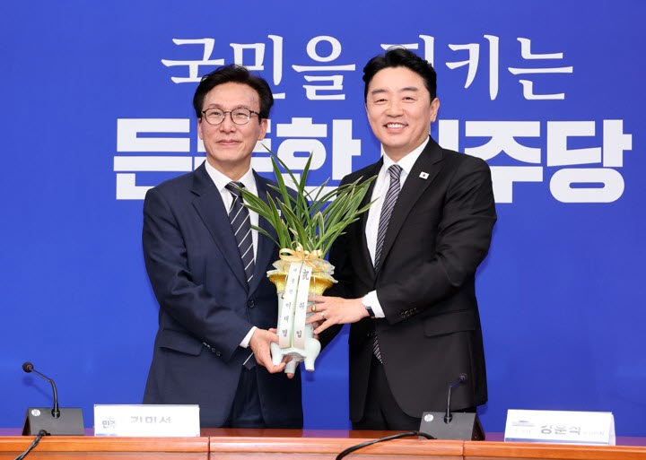 더불어민주당 김민석 대표가 18일 국회에서 취임 인사차 방문한 강훈식 대통령비서실 비서실장을 만나 이재명 대통령의 축하 난을 받고 있다.(사진=연합뉴스)