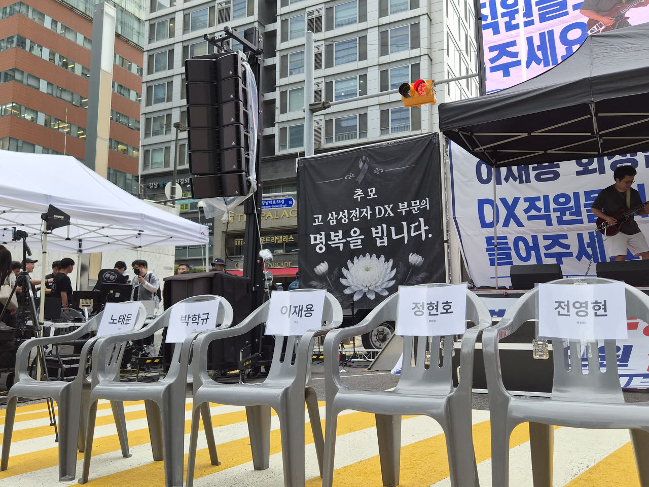21일 서울 서초구 삼성전자 서초사옥 인근에 마련된 동행노조 집회 무대 앞에 이재용 회장과 정현호 부회장 등 경영진의 이름이 붙은 빈 의자가 놓여 있다. 뒤편에는 ‘故 삼성전자 DX부문의 명복을 빕니다’라고 적힌 추모 배너가 걸려 있다. (사진=송재민 기자)