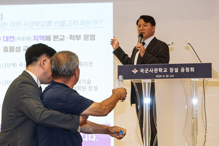 26일 서울 용산구 국방컨벤션에서 열린 국군사관학교 창설 공청회에서 한 참석자가 발언하고 있는 김홍철 국방부 정책실장에게 생수병을 들고 다가서다 저지당하고 있다. (사진=연합뉴스)