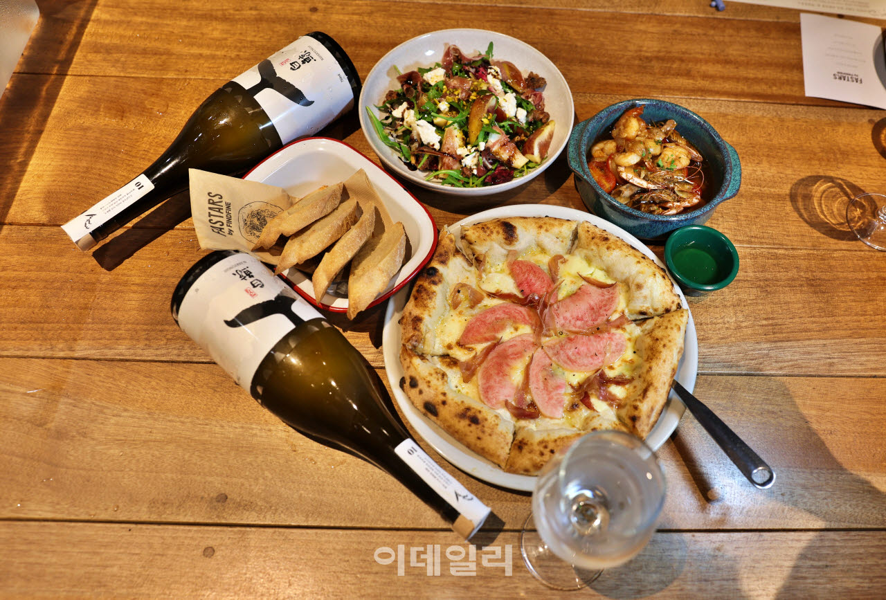 복숭아 피자와 무화과 샐러드, 감바스를 펼쳐 놓은 세종 빠스타스의 식탁. 음식 옆으로 백경증류소의 술병이 놓여 있다.(사진=이데일리 강경록 여행전문기자)