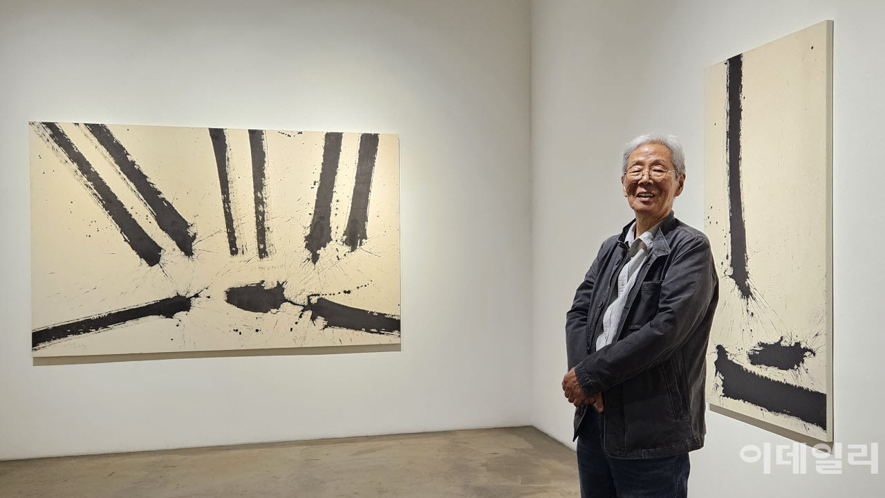 작가 김호득이 개인전 ‘-빼고 또 빼고-’에 건 자신의 작품들 앞에 서서 환하게 웃었다. 왼쪽은 ‘폭포’(2026, 250×157.7㎝), 오른쪽은 ‘폭포’(2025, 161.3×84.5㎝)(사진=오현주 문화전문기자).