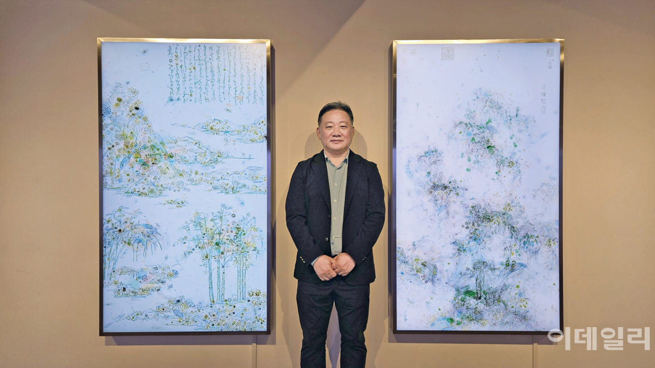 작가 이이남이 서울 종로구 학고재갤러리 개인전 ‘시어무형 청어무성’에 건 자신의 미디어 작품들 곁에 섰다. 작가의 왼쪽은 ‘미시산수-강정산색도’(2026, 170.5×97.9㎝), 오른쪽은 ‘미시산수-조춘도 no.1’(2026, 170×97.9㎝)다.