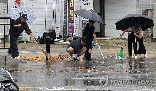 18일 경기도 고양시 일산서구에서 시민들이 낙엽이 배수구를 막아 도로가 물바다가 되자 손으로 낙엽을 걷어내고 있다. (사진=연합뉴스)