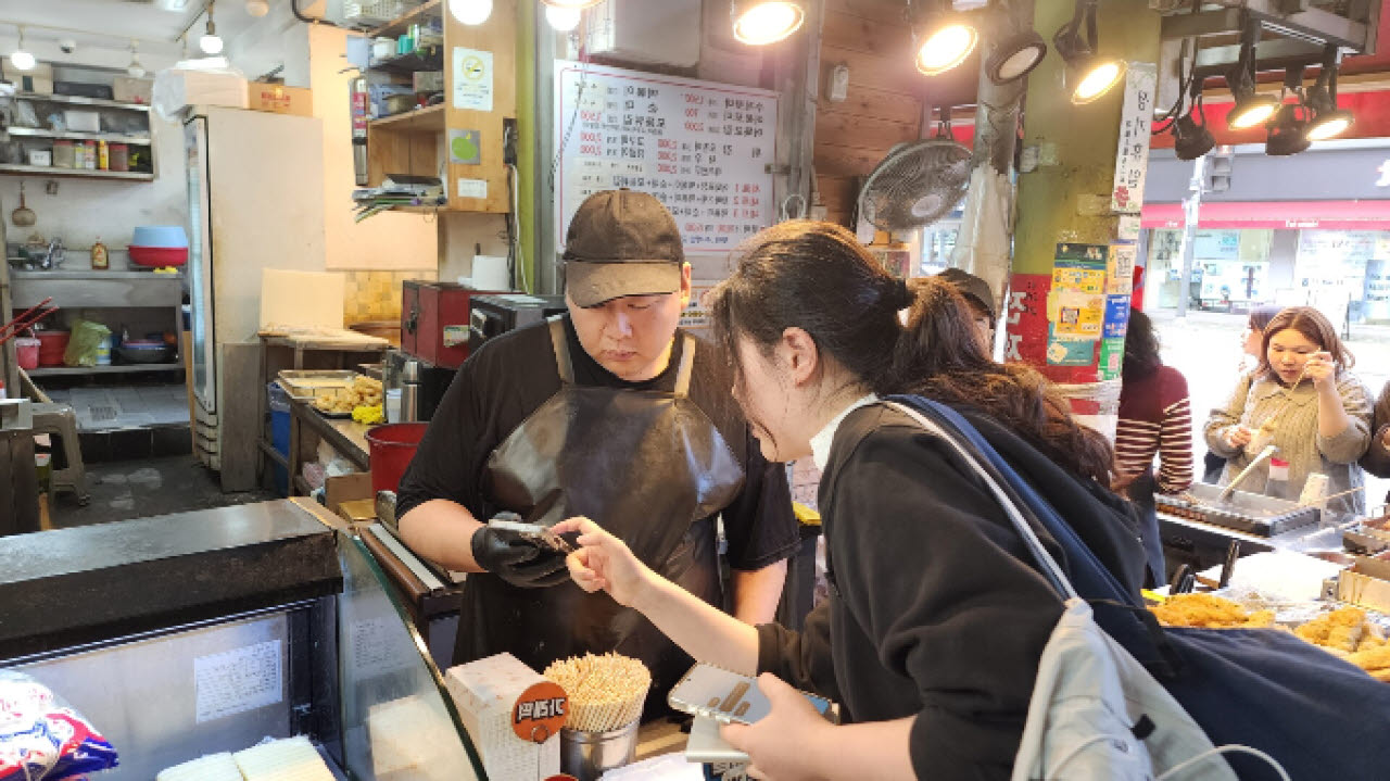 서울 마포구 망원시장의 한 점포에서 방문객과 상인이 스마트폰을 보며 대화하고 있다. 망원시장에 도입된 ‘AI 관광집사’는 외국인 관광객과 상인 간 1대1 실시간 통역을 34개 언어로 지원한다.
