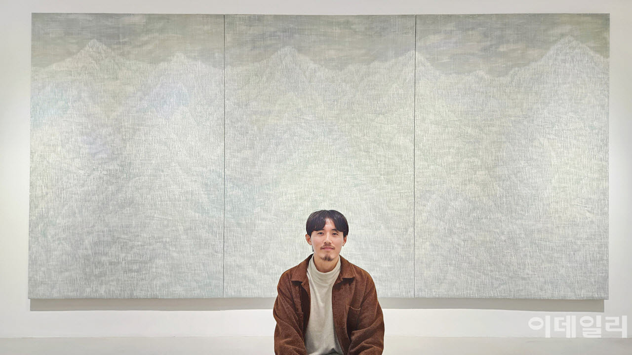 작가 우병윤이 선화랑 개인전 ‘중첩: 들떠 있는 풍경’에 건 동명의 작품 ‘중첩: 들떠 있는 풍경 26-09-330’(2026) 앞에 앉았다. 바닥에 앉아보자는 제안에 작가는 잠시의 망설임도 없었다. 120호 규모(194.0×130.3㎝) 화폭 3점을 연결한 이 대작은 수만 번 베고 갔을 그 칼끝에 남은 선과 선이 웅장한 산수를 빚고 있다. 도려낸 만큼 선명해지는 풍경이다(사진=오현주 문화전문기자).